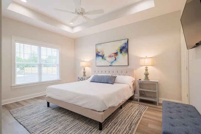 bedroom with a raised ceiling, ceiling fan, and light hardwood / wood-style floors