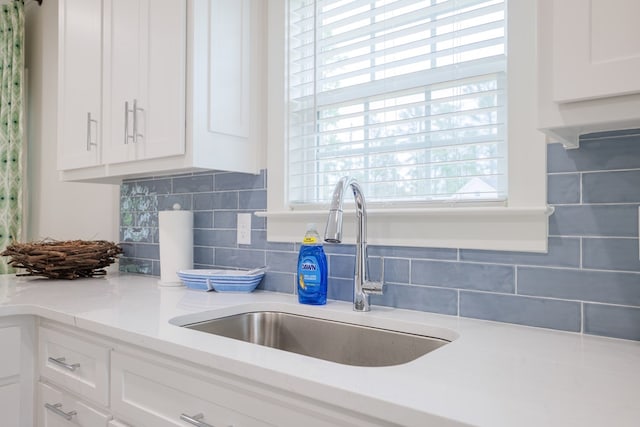 kitchen with tasteful backsplash, sink, light stone countertops, and white cabinets