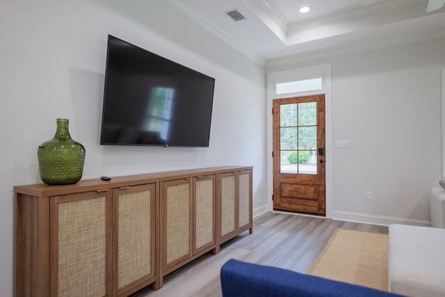 interior space featuring a raised ceiling, crown molding, and light hardwood / wood-style flooring