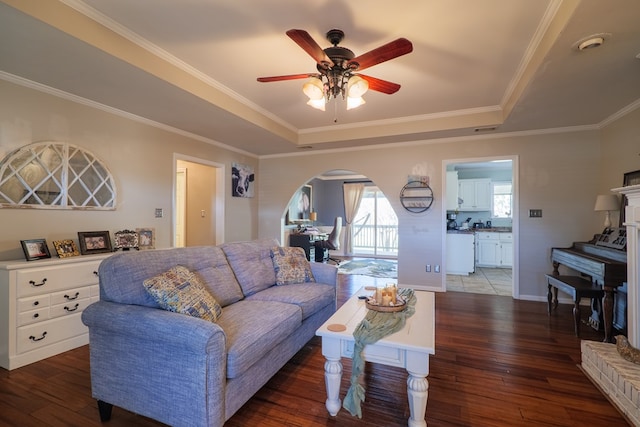 living room with a raised ceiling, ornamental molding, dark wood-type flooring, and ceiling fan