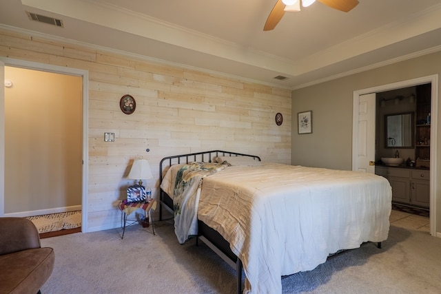 carpeted bedroom featuring wood walls, ceiling fan, a raised ceiling, crown molding, and ensuite bath