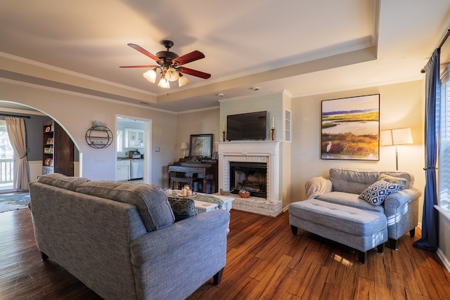 living room featuring dark hardwood / wood-style floors, a fireplace, a tray ceiling, and ceiling fan