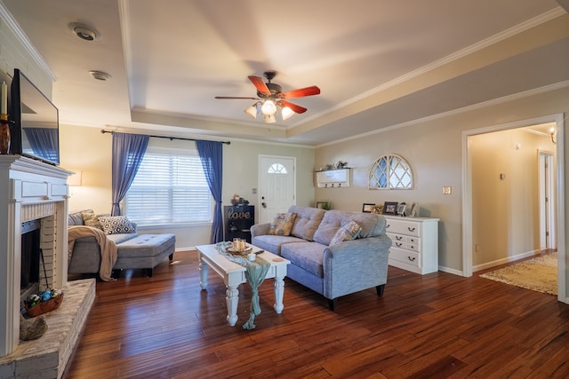 living room featuring ornamental molding, dark hardwood / wood-style flooring, a raised ceiling, and a brick fireplace