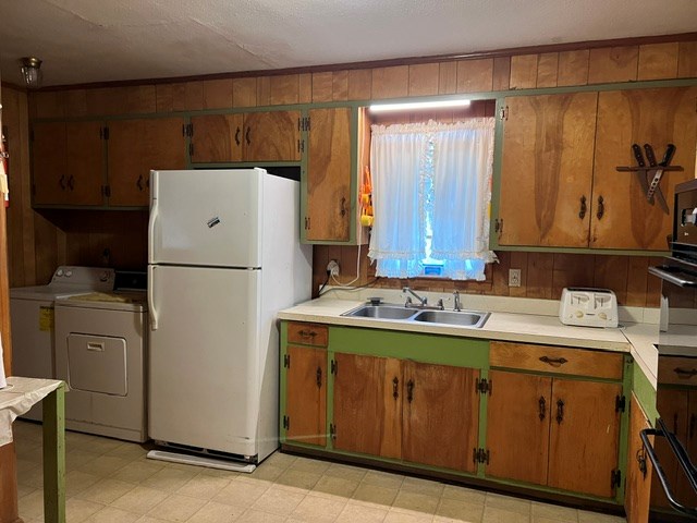 kitchen with white refrigerator, separate washer and dryer, wood walls, and sink