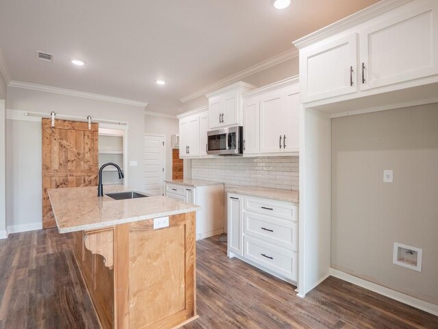 kitchen with a barn door, white cabinets, sink, and an island with sink