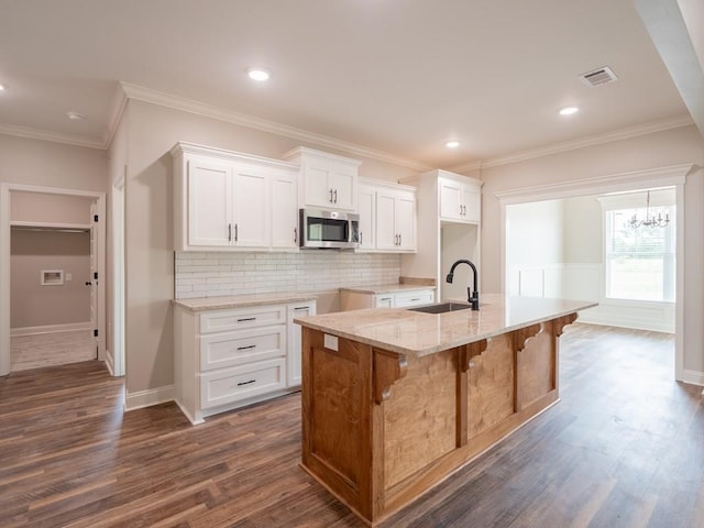 kitchen with white cabinetry, sink, a breakfast bar, a center island with sink, and ornamental molding