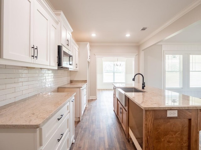 kitchen featuring a center island with sink, sink, white cabinets, and light stone counters