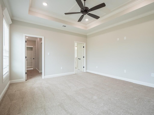 unfurnished bedroom with light carpet, a walk in closet, ceiling fan, ornamental molding, and a tray ceiling