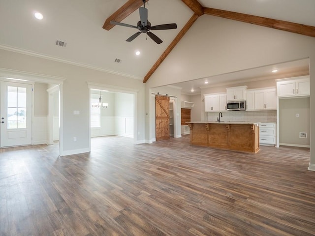 unfurnished living room with dark wood-type flooring, ceiling fan with notable chandelier, sink, a barn door, and beam ceiling