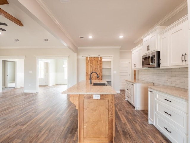 kitchen featuring crown molding, sink, a barn door, white cabinetry, and an island with sink