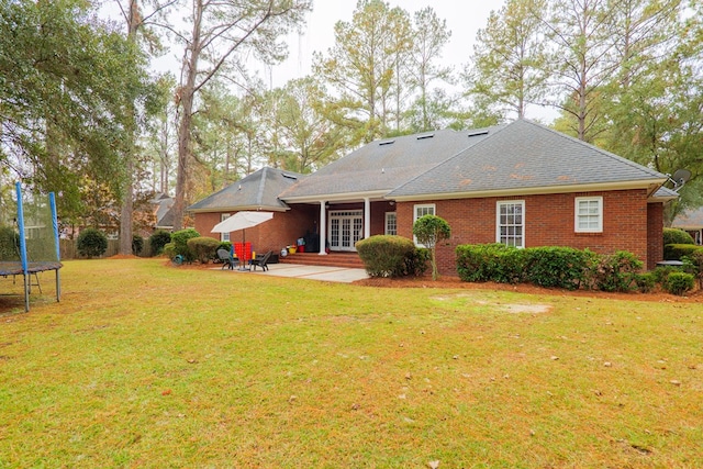 rear view of property featuring a lawn, a trampoline, a patio, and french doors