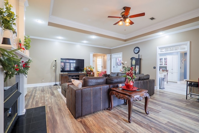 living room with ceiling fan, light hardwood / wood-style floors, crown molding, and a tray ceiling