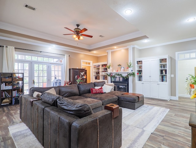 living room featuring ceiling fan, ornate columns, light wood-type flooring, ornamental molding, and a tray ceiling