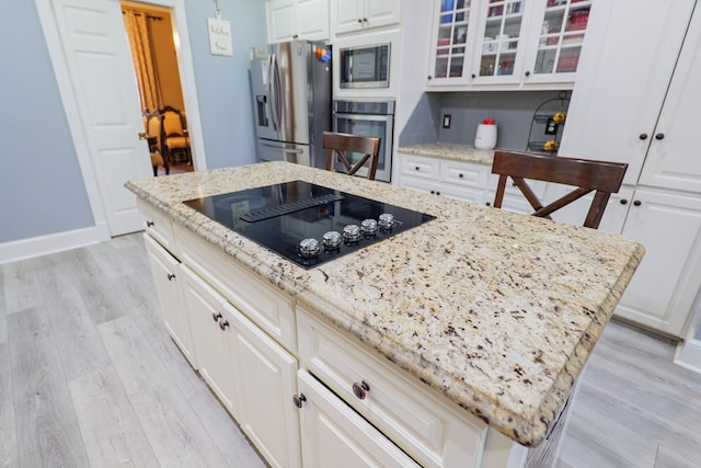 kitchen with light stone countertops, light hardwood / wood-style flooring, a kitchen island, and appliances with stainless steel finishes