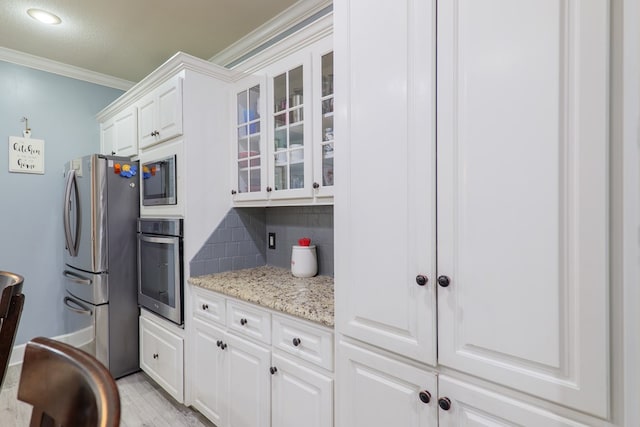 kitchen with light stone countertops, appliances with stainless steel finishes, backsplash, crown molding, and white cabinetry