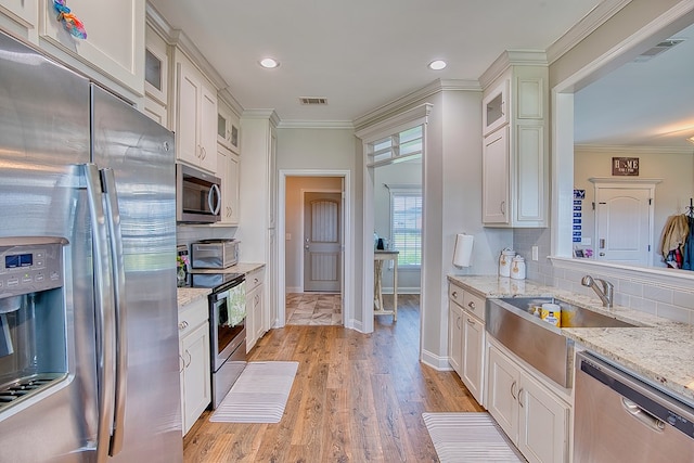 kitchen featuring a sink, decorative backsplash, stainless steel appliances, white cabinetry, and visible vents
