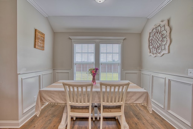 dining area featuring vaulted ceiling, a wainscoted wall, wood finished floors, and a decorative wall