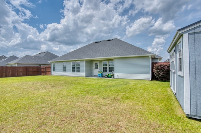 back of property with a yard, a shingled roof, and fence