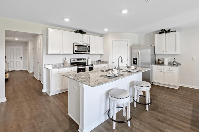 kitchen featuring dark wood-style floors, a breakfast bar, stainless steel appliances, white cabinetry, and a sink