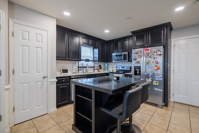 5187 Calvary Cir, Valdosta, GA 31605 - kitchen with stainless steel appliances, light tile patterned floors, dark cabinetry, decorative backsplash, and a kitchen bar