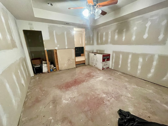 interior space with ceiling fan, a tray ceiling, and concrete flooring