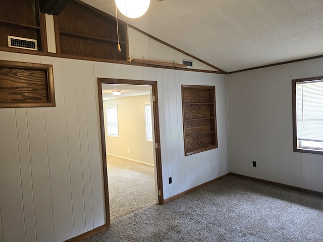 carpeted empty room with lofted ceiling, visible vents, and wood walls