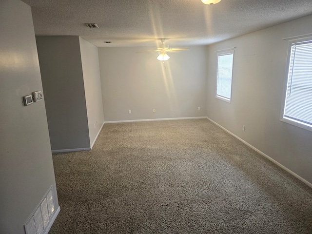 carpeted empty room featuring a textured ceiling, baseboards, a ceiling fan, and visible vents