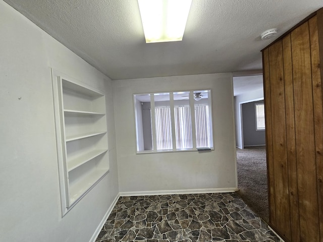 unfurnished room featuring a textured ceiling, baseboards, stone finish flooring, and built in shelves