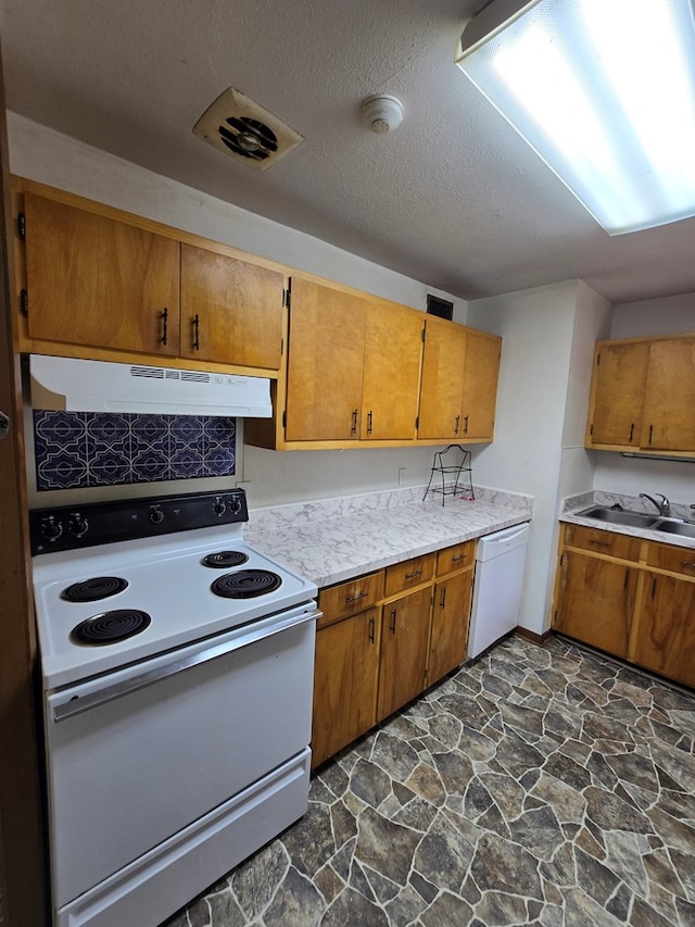 kitchen featuring stone flooring, under cabinet range hood, white appliances, a sink, and light countertops