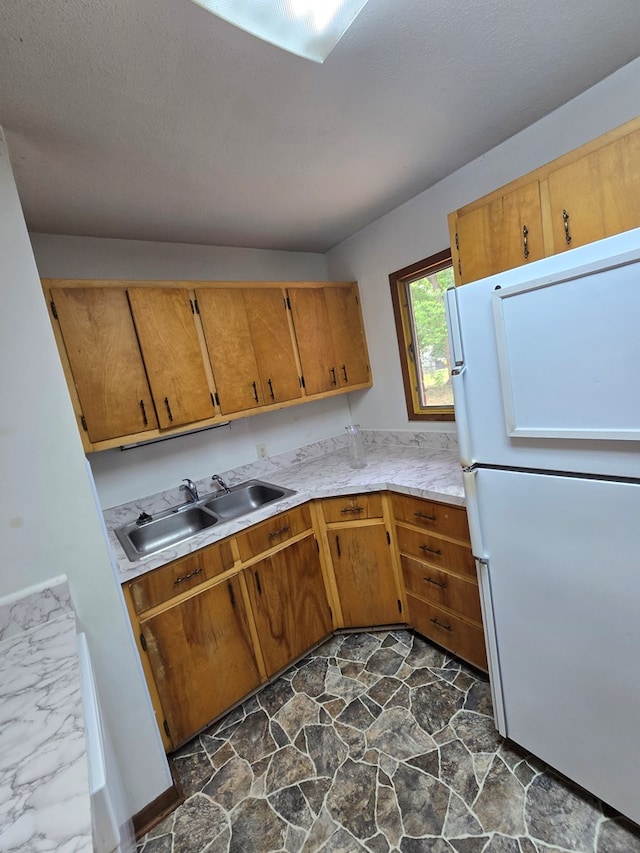 kitchen featuring a sink, brown cabinets, freestanding refrigerator, light countertops, and stone flooring