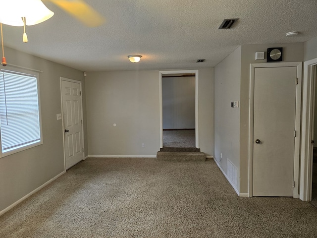 carpeted empty room featuring a textured ceiling, baseboards, and visible vents