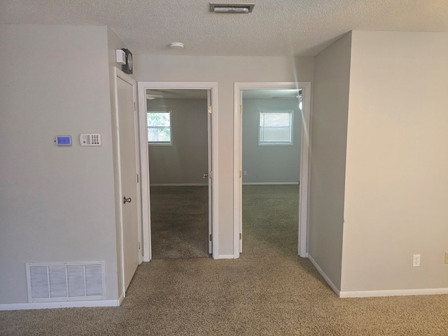 hallway with a healthy amount of sunlight, carpet flooring, and visible vents