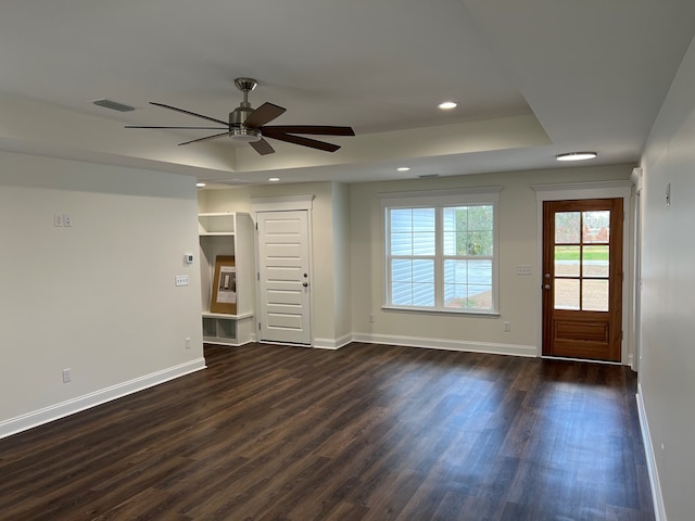 unfurnished room featuring a tray ceiling, ceiling fan, and dark wood-type flooring