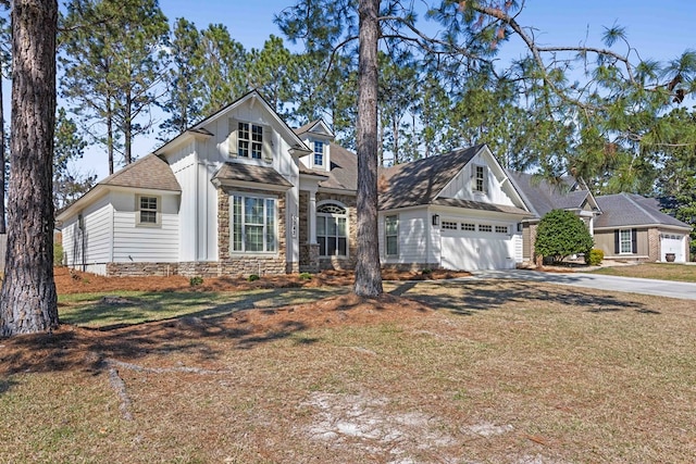 view of front facade featuring driveway, stone siding, an attached garage, and a front yard