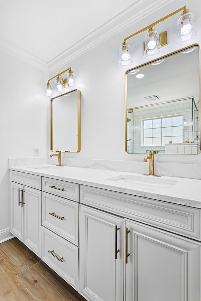 full bath with wood finished floors, double vanity, ornamental molding, and a sink