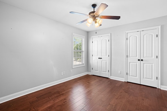 unfurnished bedroom with dark wood-style floors, ceiling fan, baseboards, and two closets