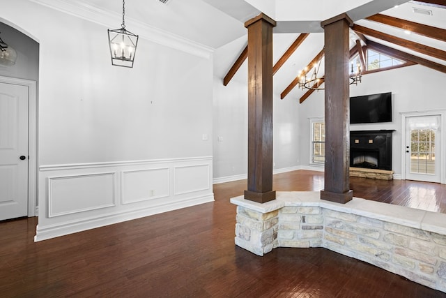 unfurnished living room featuring a fireplace with raised hearth, a notable chandelier, dark wood-type flooring, beamed ceiling, and decorative columns