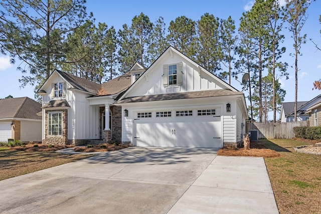 view of front of property with board and batten siding, fence, a garage, stone siding, and driveway