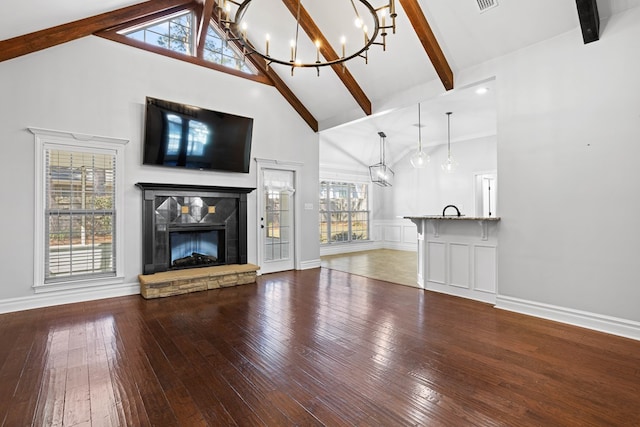 unfurnished living room featuring a chandelier, hardwood / wood-style floors, a fireplace, high vaulted ceiling, and beam ceiling