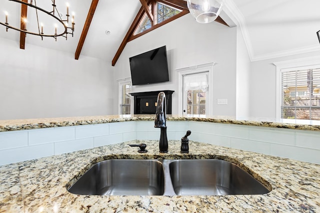 kitchen featuring beamed ceiling, a sink, a wealth of natural light, and light stone countertops