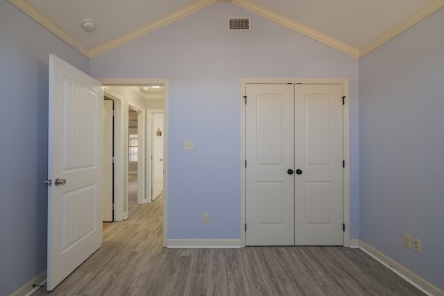 unfurnished bedroom with crown molding, vaulted ceiling, a closet, and light wood-type flooring