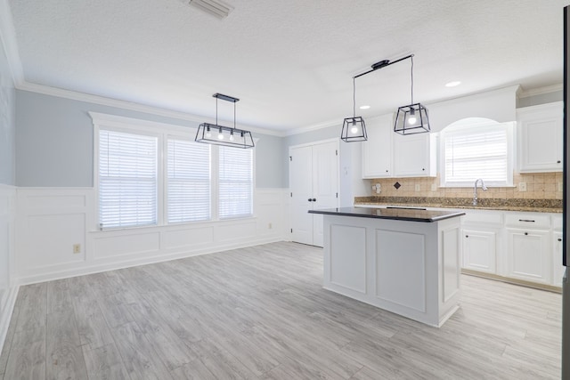 kitchen with white cabinetry, a center island, ornamental molding, light hardwood / wood-style floors, and decorative light fixtures