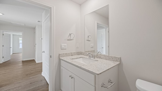 bathroom featuring visible vents, baseboards, toilet, wood finished floors, and vanity