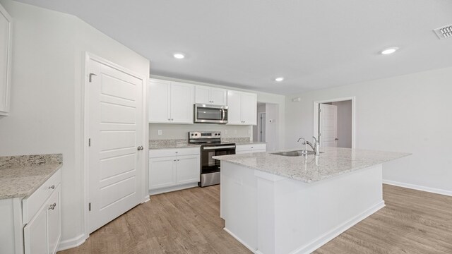 kitchen with appliances with stainless steel finishes, light wood-type flooring, white cabinetry, and a sink