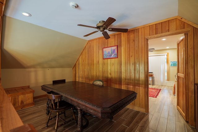 dining room featuring ceiling fan, hardwood / wood-style floors, wood walls, and lofted ceiling