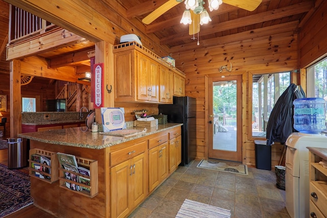 kitchen featuring black fridge, light stone counters, wooden walls, wooden ceiling, and beamed ceiling