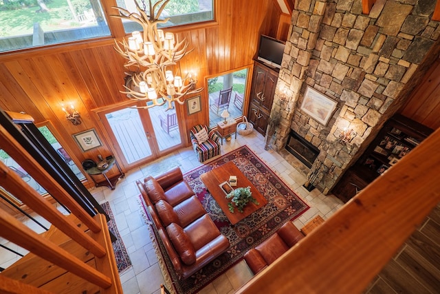 living room with a notable chandelier, wood walls, a stone fireplace, and a towering ceiling