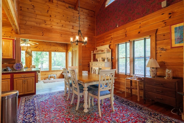 dining space featuring beamed ceiling, high vaulted ceiling, wood walls, wood-type flooring, and ceiling fan with notable chandelier