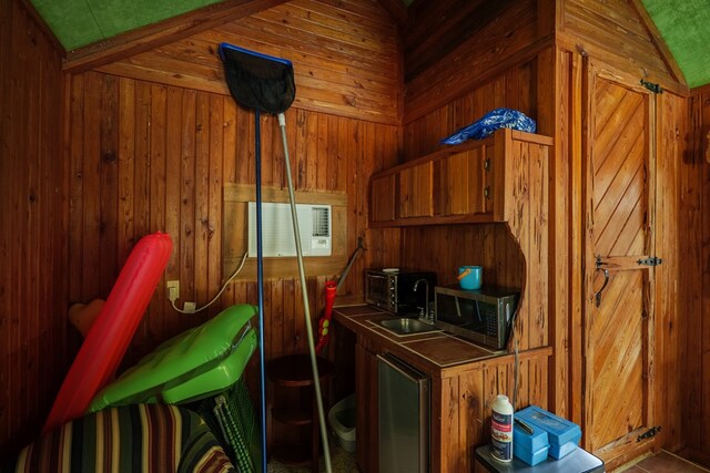 kitchen featuring a wall mounted AC, wood walls, sink, and vaulted ceiling