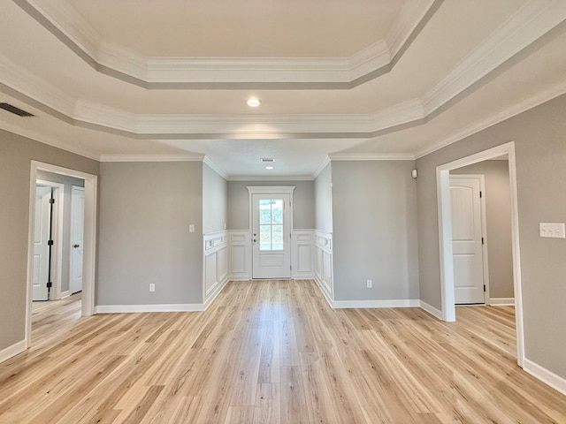 spare room with visible vents, a tray ceiling, ornamental molding, wainscoting, and light wood-type flooring